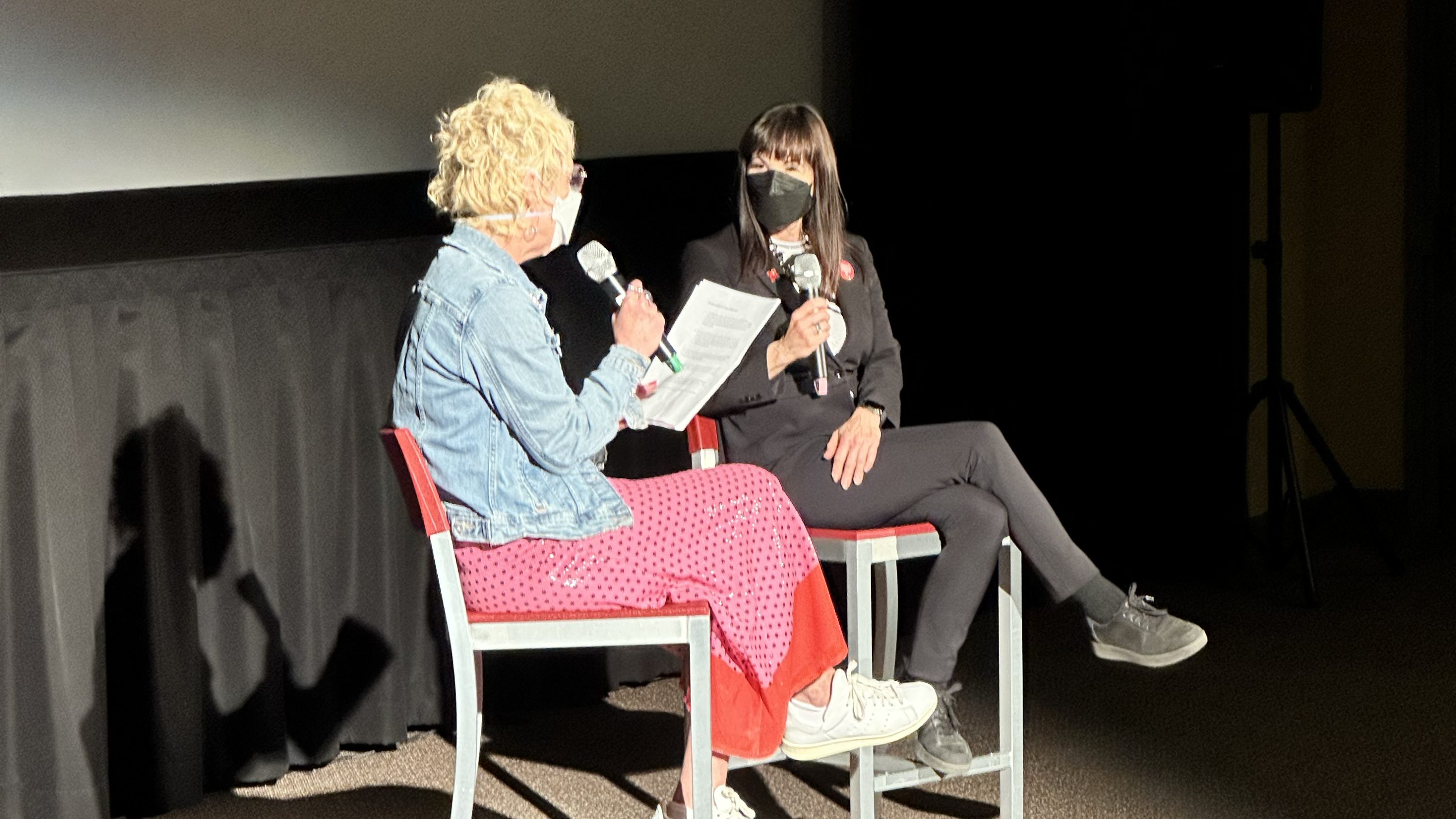 Two people in chairs on stage with microphones talking to each other