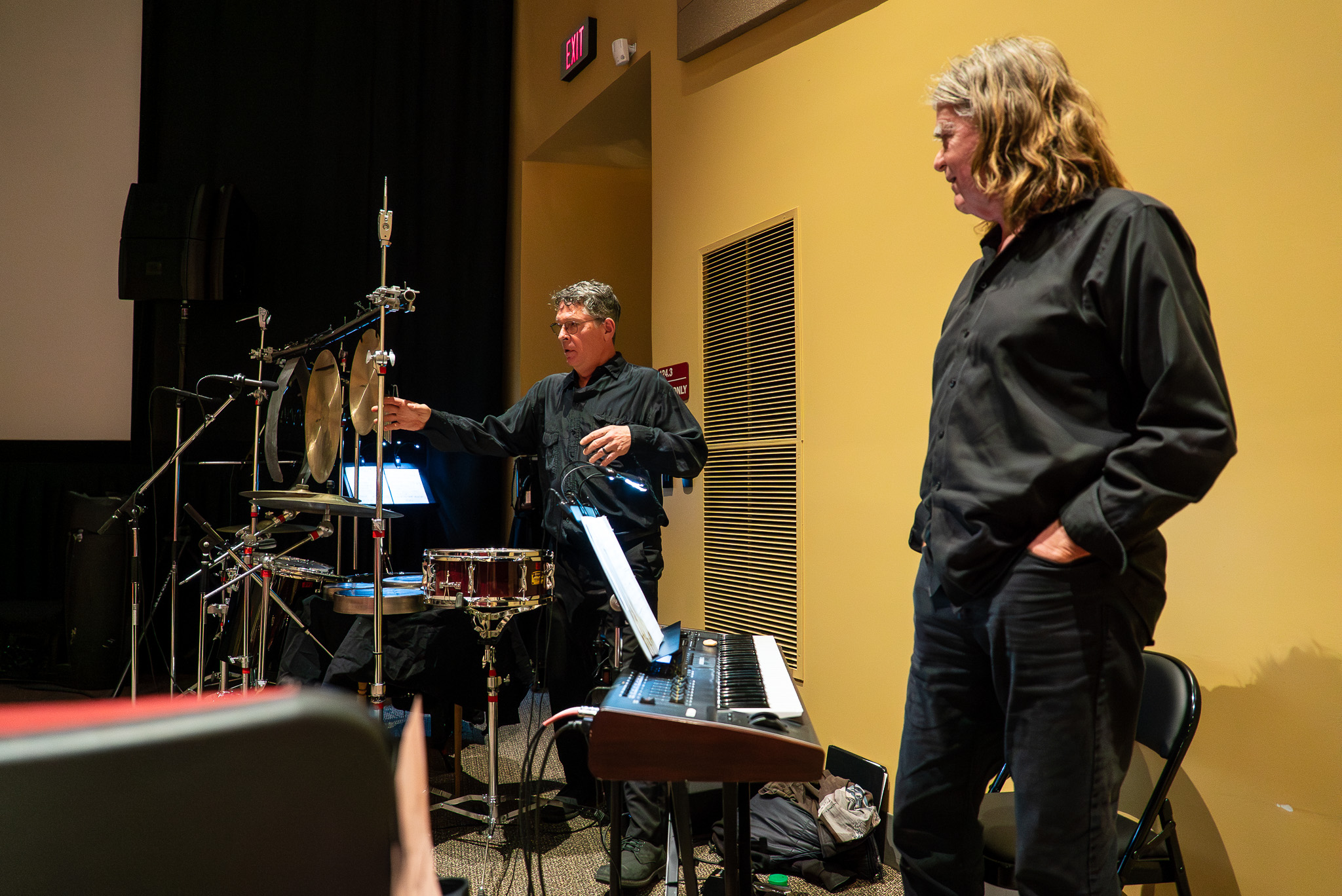 Two people dressed in all black standing amongst instruments