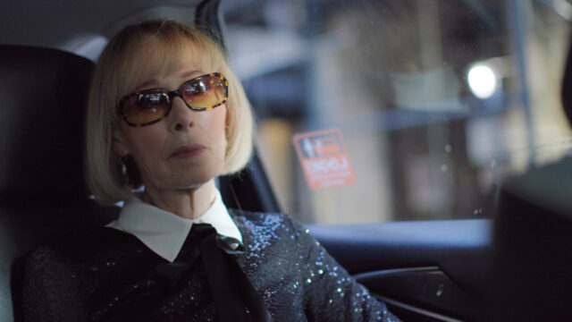 Older blonde woman in black sequins and sunglasses is passenger in a car.
