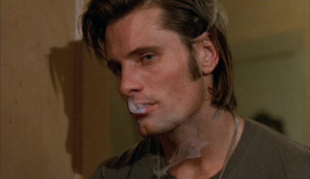 Good looking man with medium length, swept back hair exhales cigarette smoke and inhales it back into his nose.