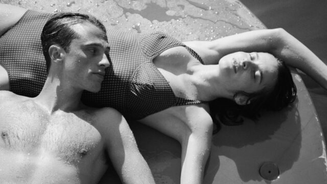 A man and woman lay on the ground near a pool. The man's head is resting on the woman's stomach.