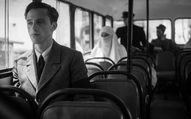 A man in a suit looks out the window while sitting in a nearly empty bus.