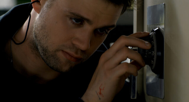 A scene from Tuner. Niki (Leo Woodall) rests his ear against a safe while turning the dial.