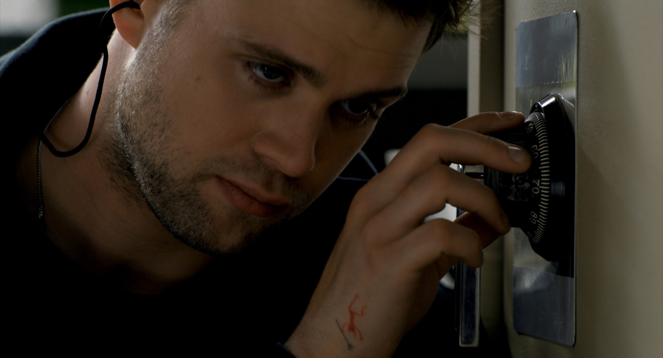 A scene from Tuner. Niki (Leo Woodall) rests his ear against a safe while turning the dial.