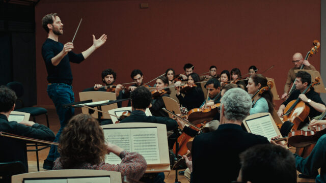 Benjamin Lavernhe stars as Thibaut Desormeaux in Emmanuel Courcol’s THE MARCHING BAND. A man in jeans and a t-shirt conducts an orchestra.