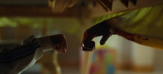 A childs hand reaches towards an ape's hand in a scene from Nope.