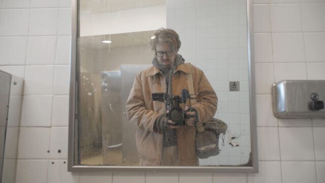 Filmmaker John Wilson holds a camera pointed into a mirror in a scene from The History of Concrete.