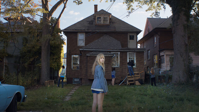 Maika Monroe and other teenagers stand around an old house in a scene from It Follows.