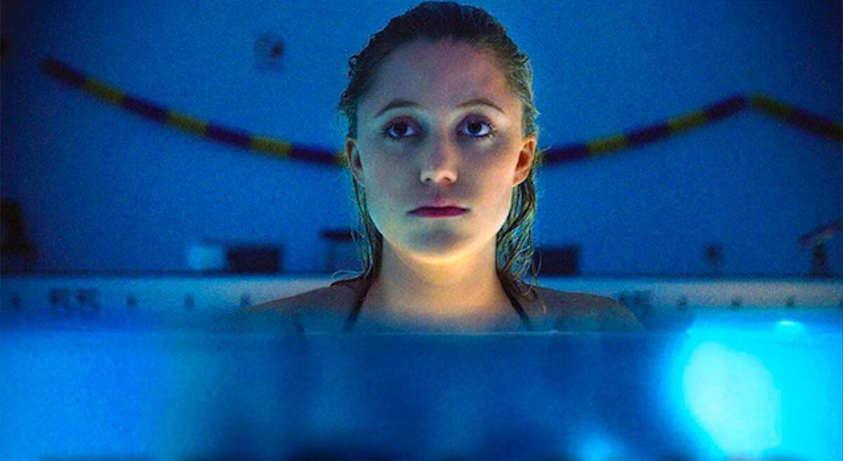 Maika Monroe looks nervously while standing in a dimly lit swimming pool in a scene from It Follows.