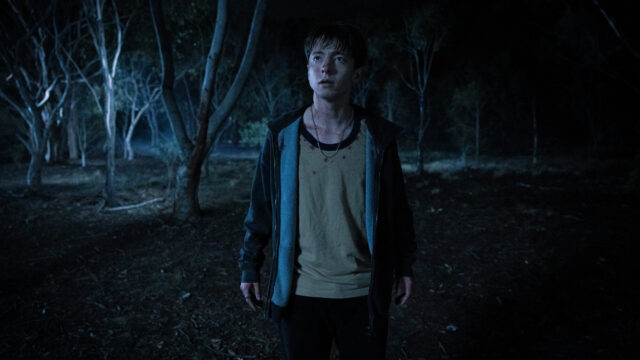 A frightened teen boy (Joe Bird) stands in a dark forest in a scene from Leviticus.