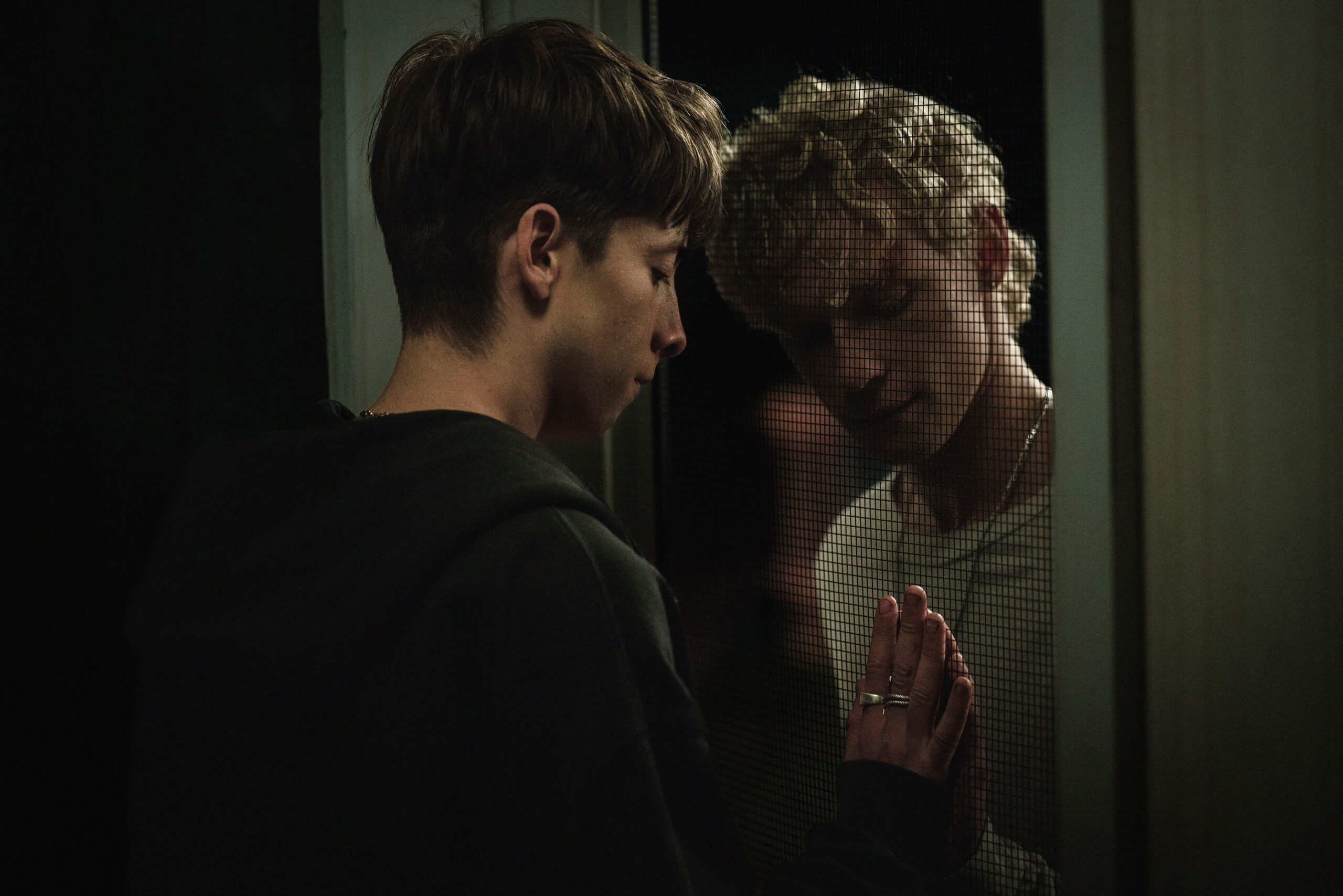 Two teen boys (Joe Bird, Stacy Clausen) touch hands across a screen door in a scene from Leviticus.