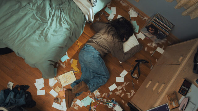A woman lies on the floor near a bed in a scene from the short film The Sixth.