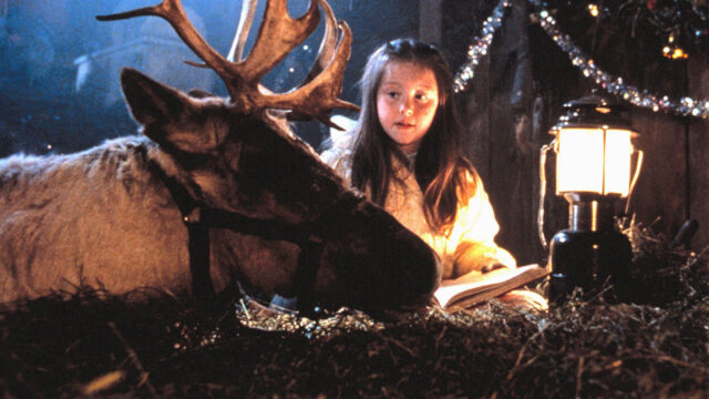 A young girl sits with a reindeer in a scene from Prancer.